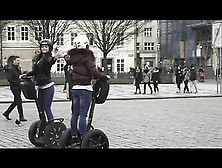 Two Sexy Brunette Girls Ride Segways In Park Square While Wearing Coats.