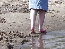 On High Heels And Bare Feet On The Sand,  Plump Legs Walk Along The Shore.